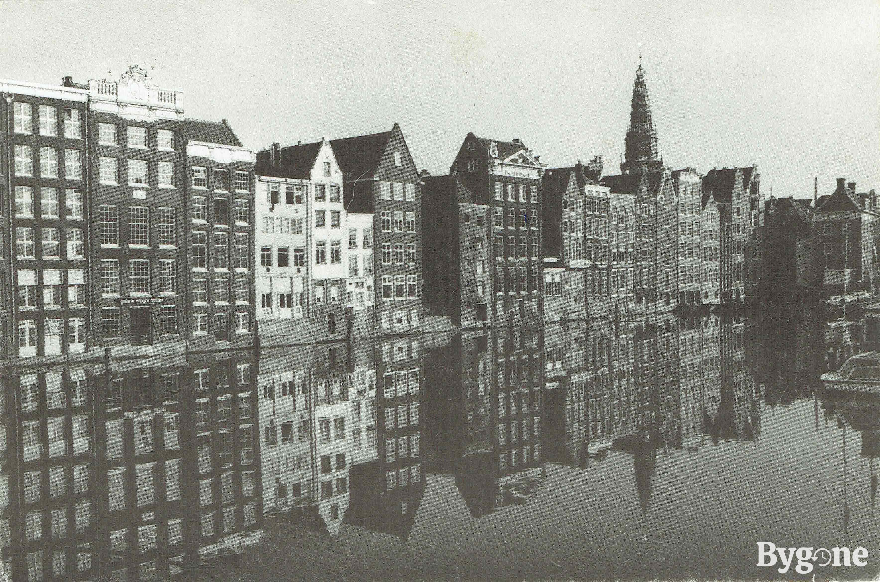 A beautiful mirror image in black and white of a row of waterfront townhouses reflected in the water of a still canal.